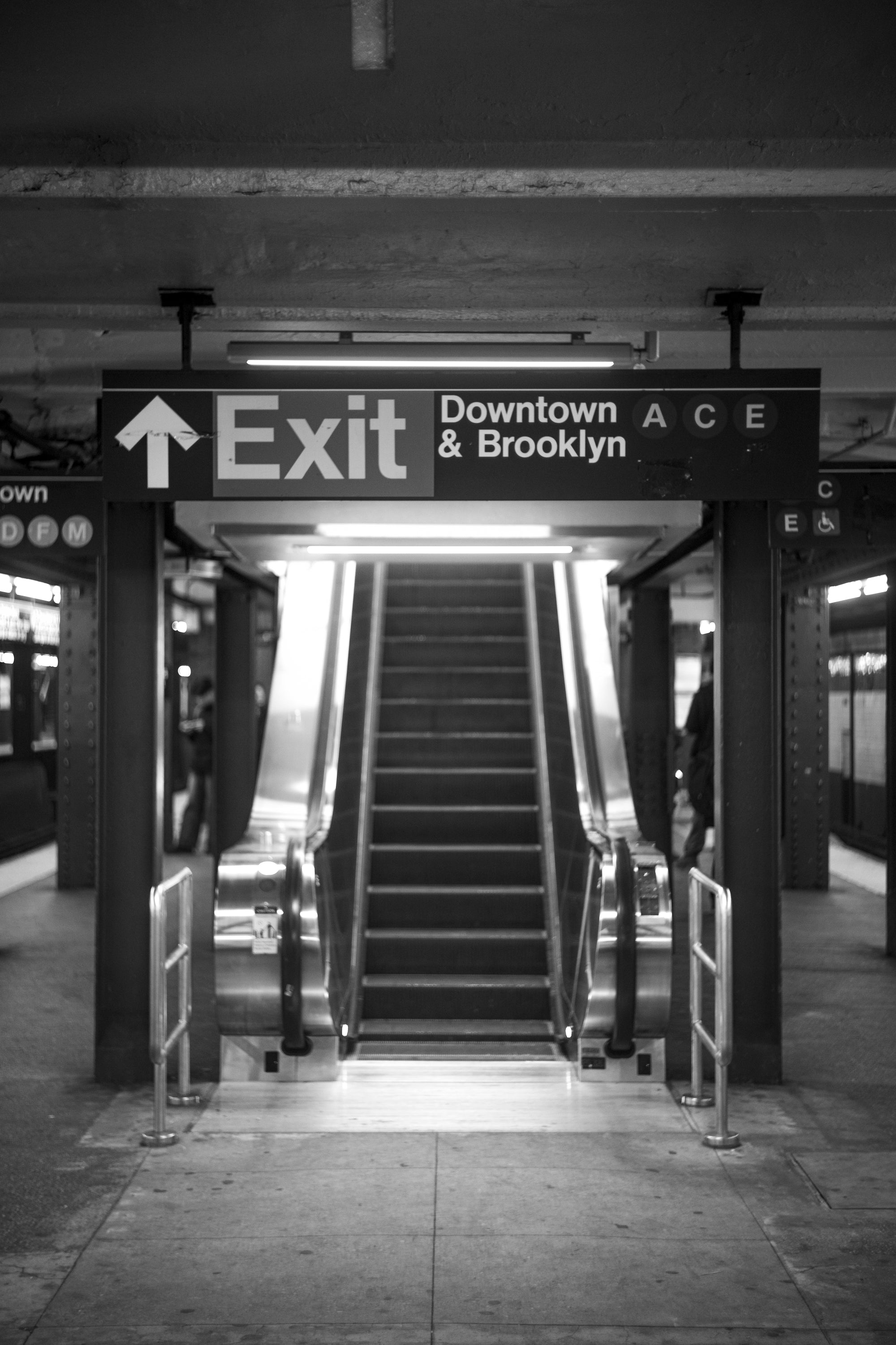 Black-and-white photograph of an empty NYC subway escalator under the Downtown & Brooklyn ACE exit sign at 3am, Portals series.