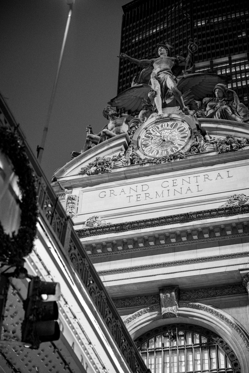Black-and-white photo of the Mercury, Hercules, and Minerva sculpture group above the Grand Central Terminal clock and entablature, NYC.