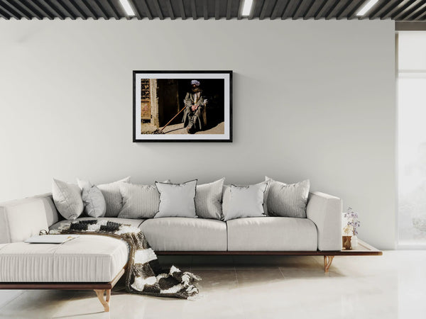 Egypt Old Man with Cane, Cairo's Garbage City framed in black above a terracotta velvet sofa, gray plaster wall — Good Beans NYC.