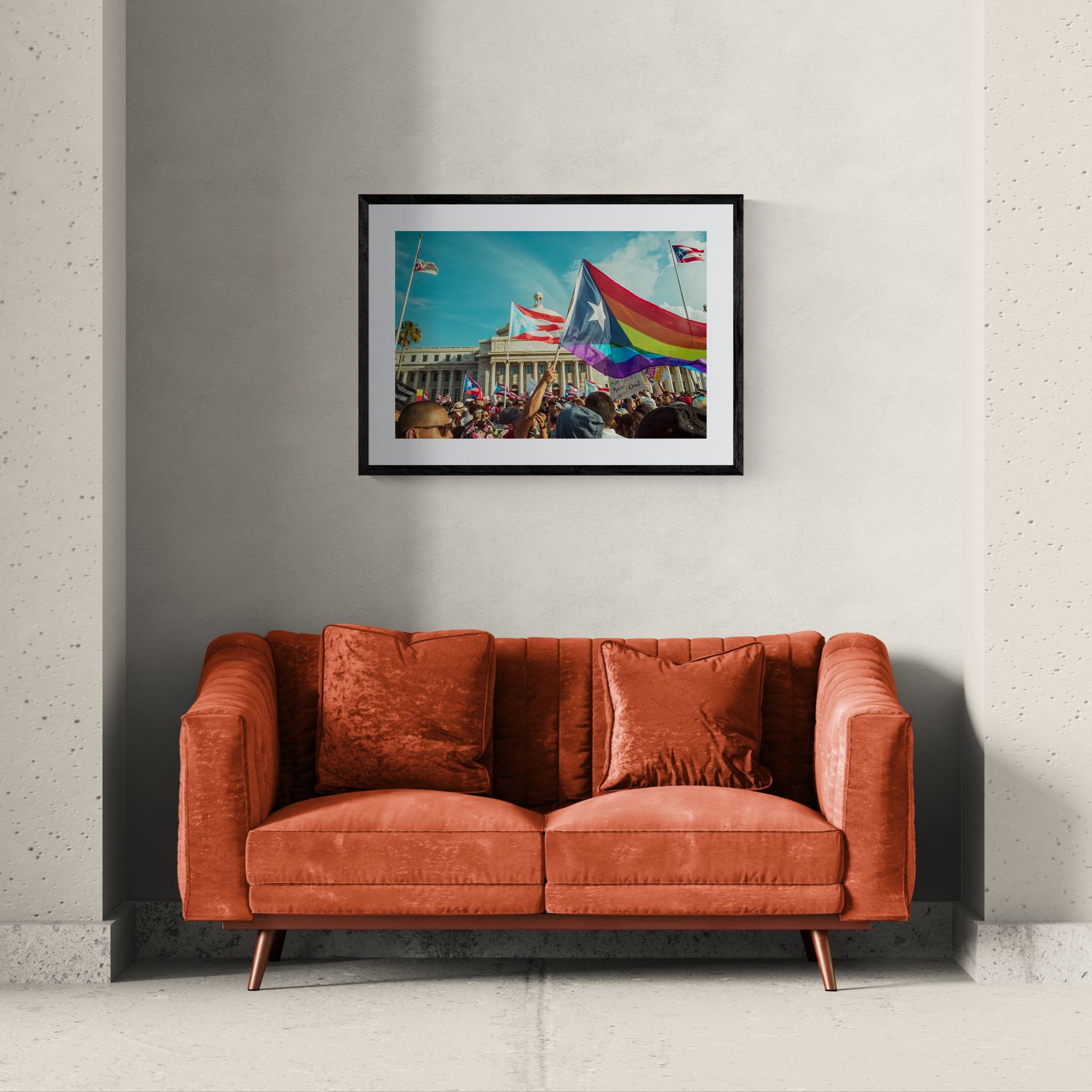 Puerto Rico Capitol Pride Protest, Rainbow Flag framed in black above a terracotta velvet sofa, gray plaster wall — Good Beans NYC.