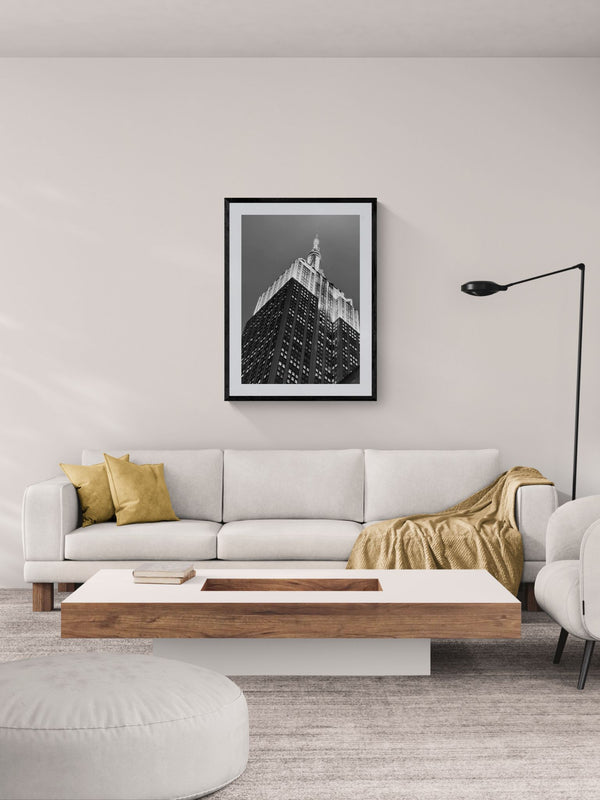 NYC Empire State Building, A Different Angle framed in black above a beige sofa, sunlit yellow plaster wall — Good Beans NYC.