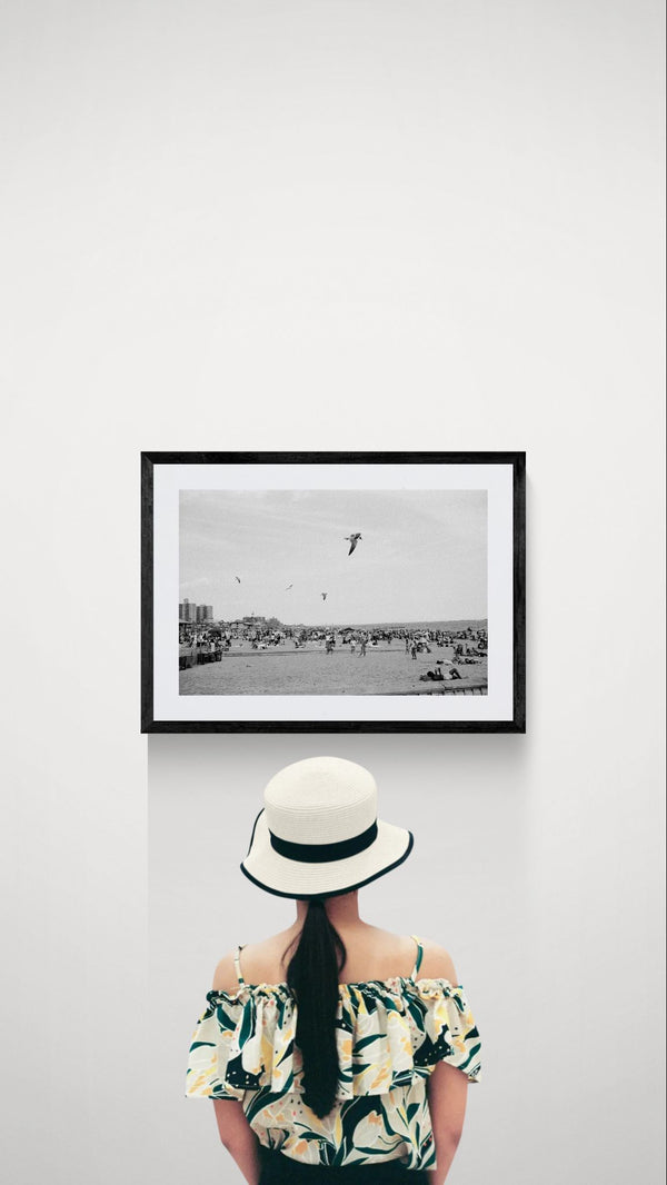 NYC Coney Island Beach Birds, Brooklyn framed in black on a gallery wall with a viewer in a straw hat in front — Good Beans NYC.