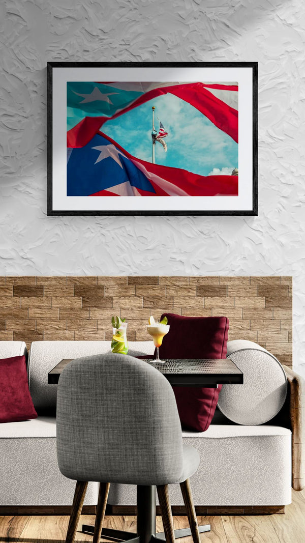 Puerto Rican Flag, American Flag at Half Mast, San Juan framed in black above a beige sofa, sunlit yellow plaster wall — Good Beans NYC.