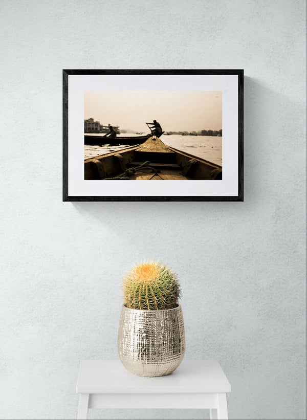 Dhaka Rower at Sunrise, Buriganga River framed in black above a terracotta velvet sofa, gray plaster wall — Good Beans NYC.