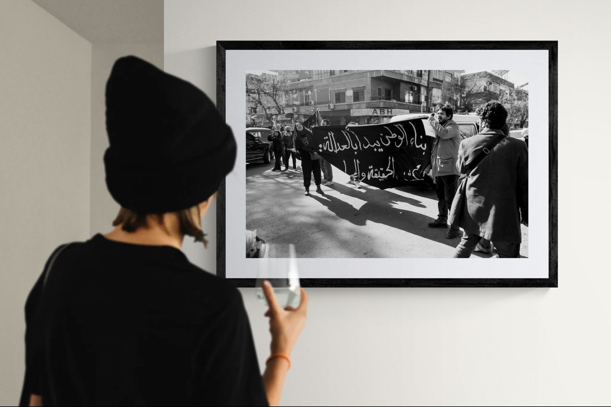 Damascus Justice Banner Protest, Syria framed in black on a gallery wall with a viewer in a straw hat in front — Good Beans NYC.