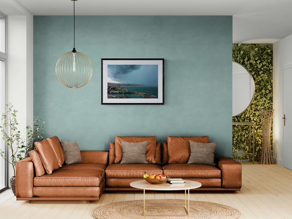 Beirut Storm, Lebanese Coast framed in black above a brown leather sectional, teal wall, gold pendant lamp — Good Beans NYC.