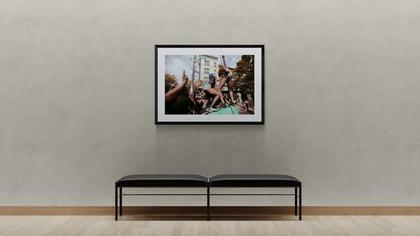 NYC J'Ouvert Twerking, Nostrand Avenue framed in black on a gallery wall with a viewer in a straw hat in front — Good Beans NYC.