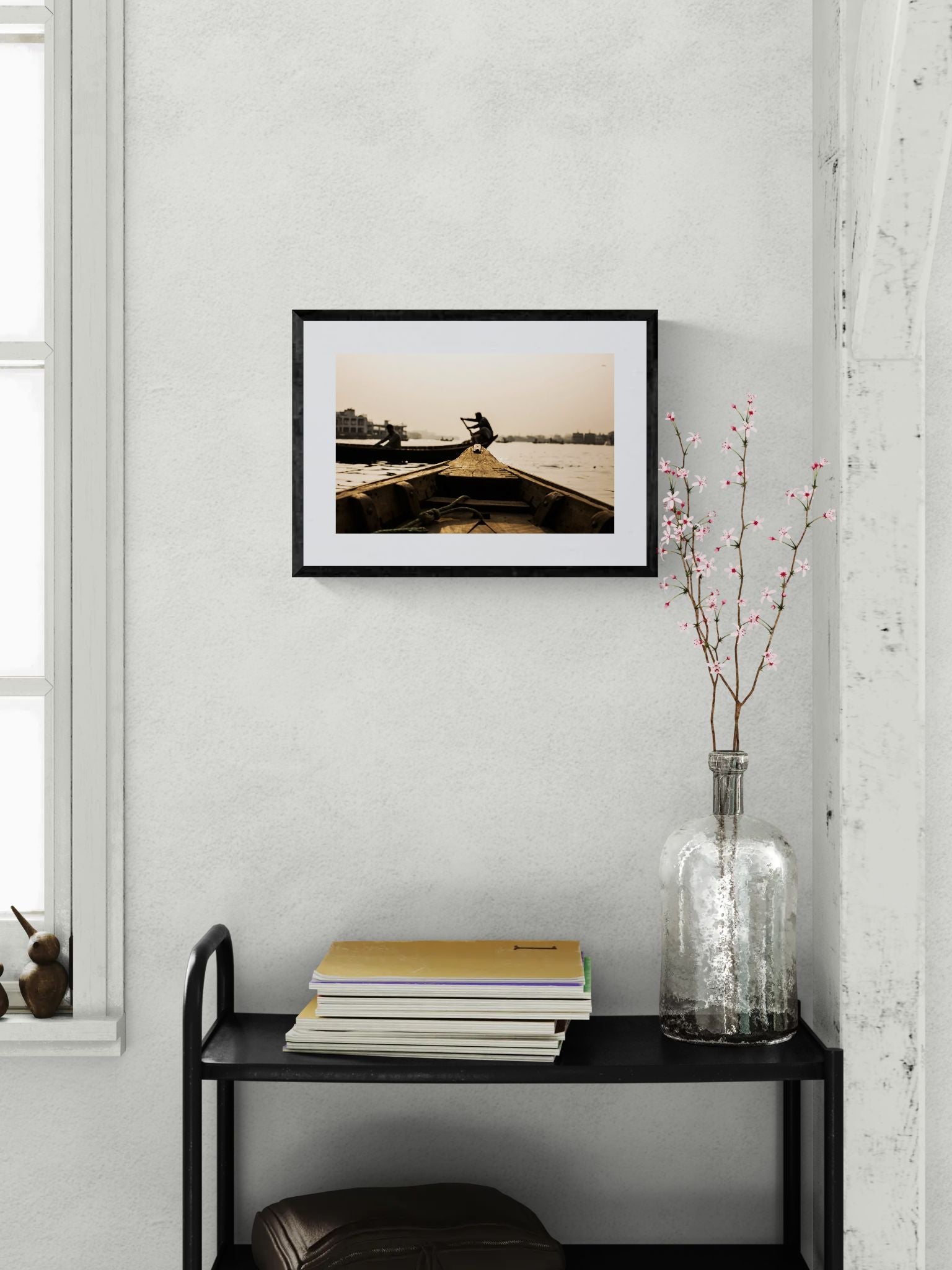Dhaka Rower at Sunrise, Buriganga River framed in black on a gallery wall with a viewer in a straw hat in front — Good Beans NYC.
