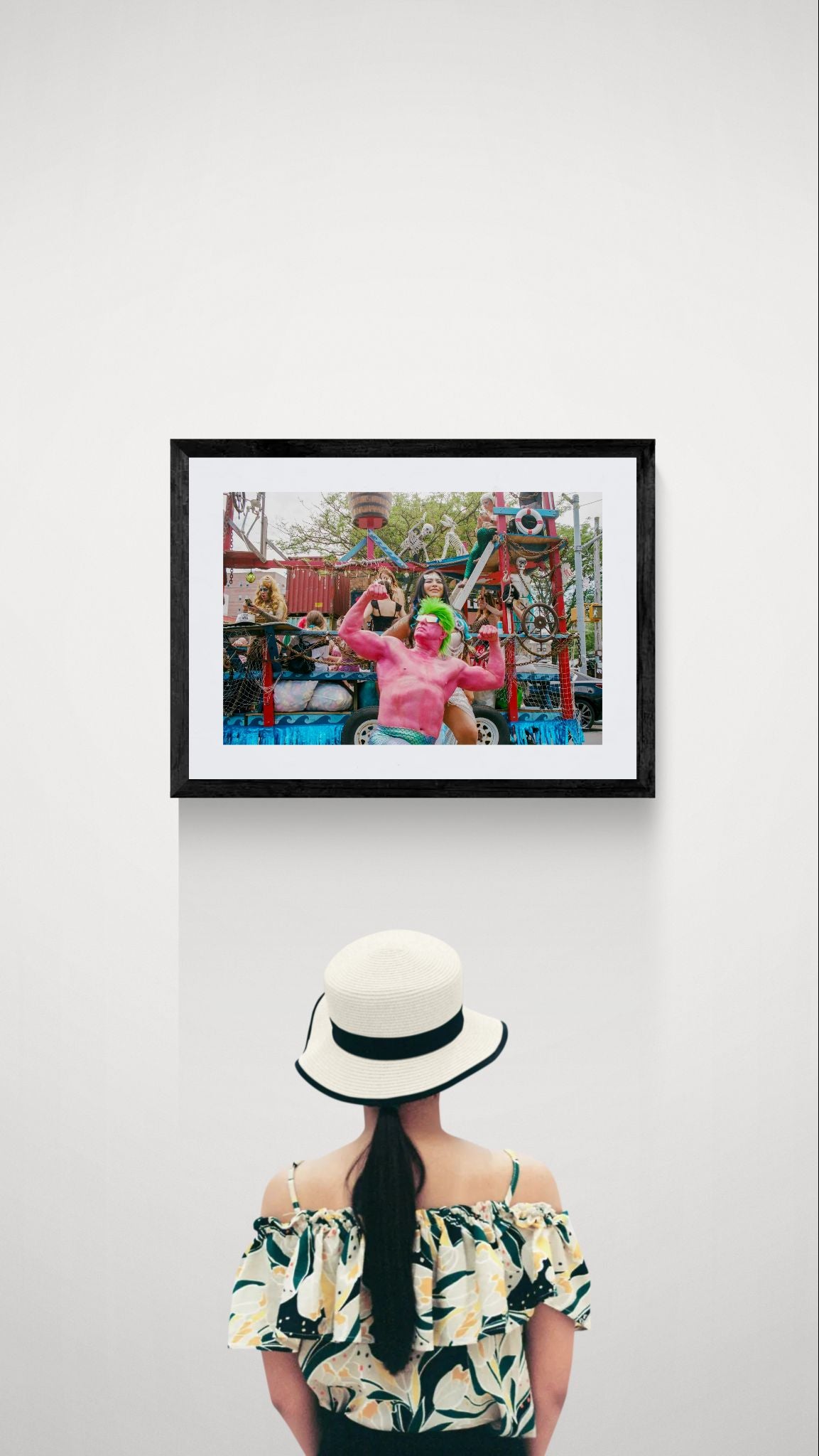 NYC Mermaid Parade Pink Hulk — Coney Island framed in black on a gallery wall with a viewer in a straw hat in front — Good Beans NYC.