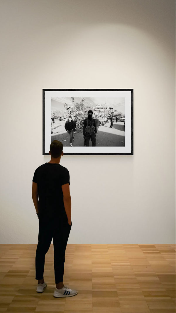 Damascus Masked Armed Fighter at Protest, Syria framed in black on a gallery wall with a viewer in a straw hat in front — Good Beans NYC.