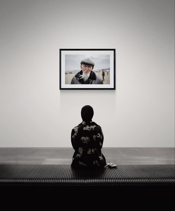 Old Mongolian Man Portrait, Bayan-Ölgii framed in black on a gallery wall with a side-profile viewer in a dark coat — Good Beans NYC.