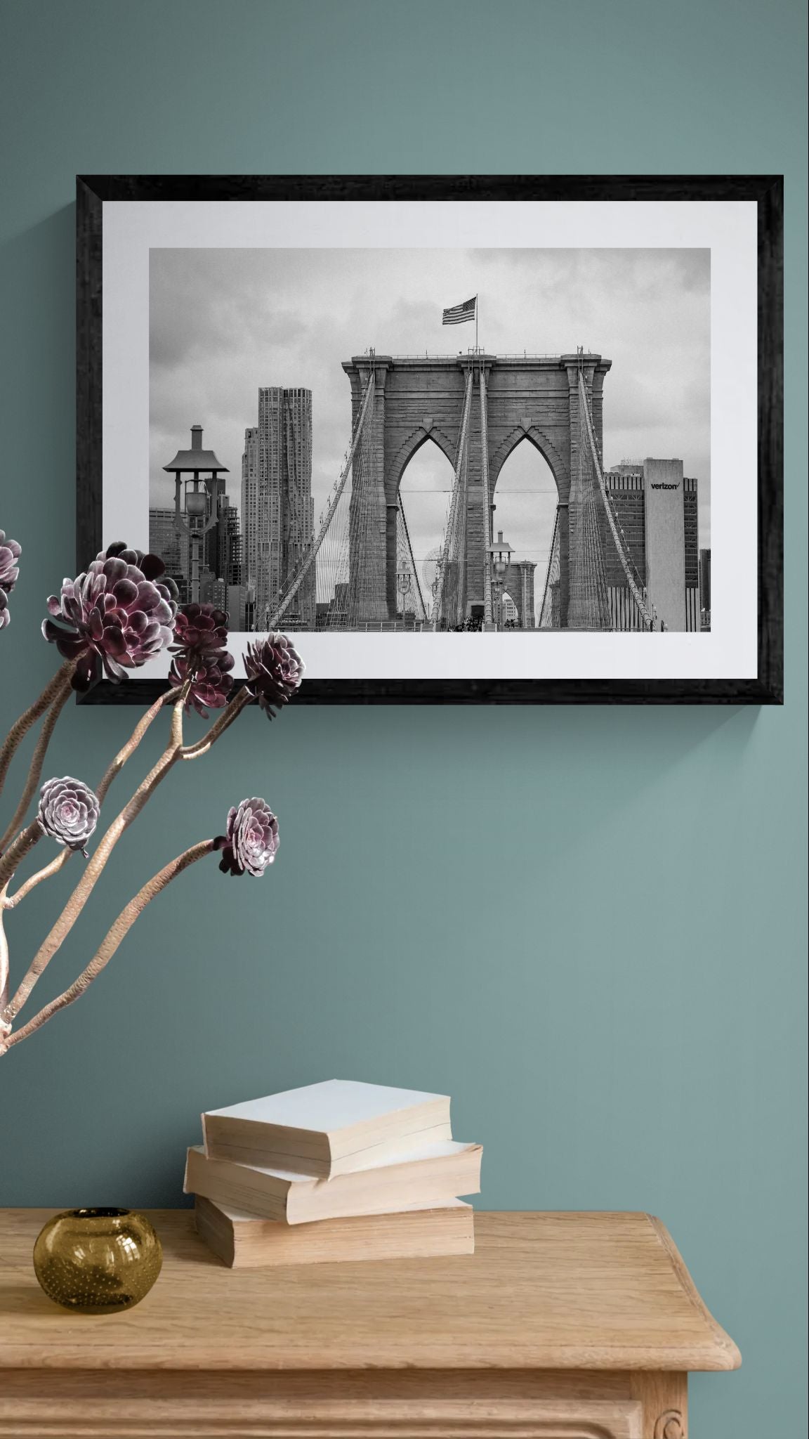 NYC Brooklyn Bridge from Afar, Manhattan Skyline framed in black on a gallery wall with a side-profile viewer in a dark coat — Good Beans NYC.