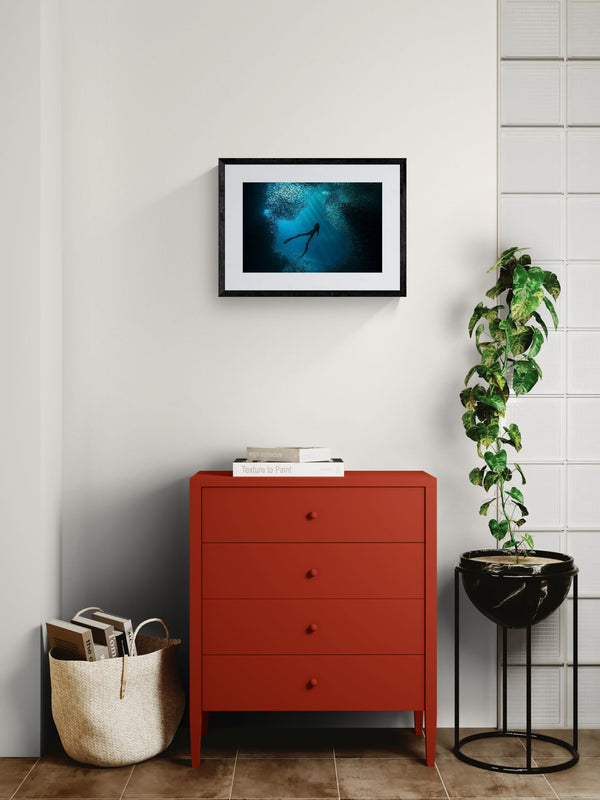 Free Diver Off Mexico Coast, Photo by Karim Iliya framed in black above a beige sofa, sunlit yellow plaster wall — Good Beans NYC.