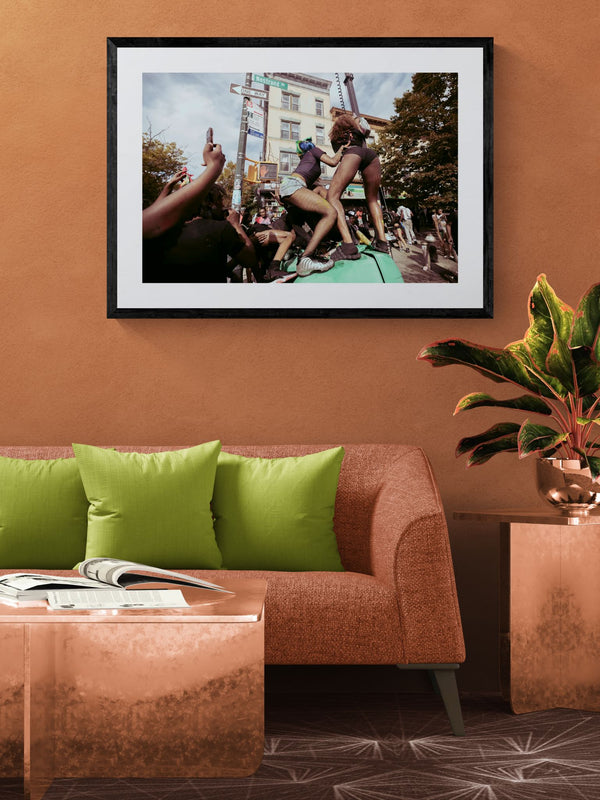 NYC J'Ouvert Twerking, Nostrand Avenue framed in black above a beige sofa, sunlit yellow plaster wall — Good Beans NYC.