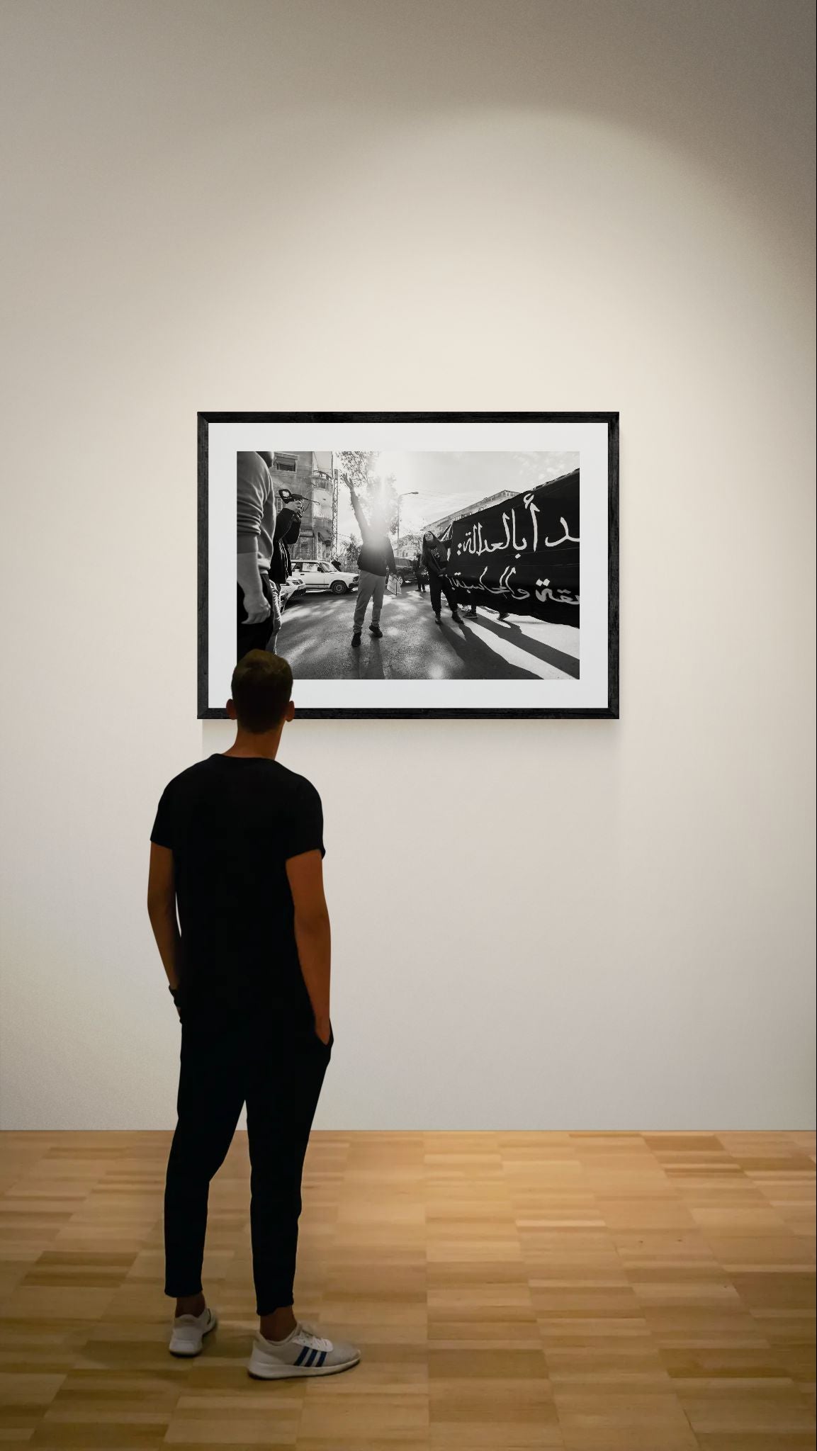 Damascus Raised Fist Protest, Syria framed in black on a gallery wall with a viewer in a straw hat in front — Good Beans NYC.