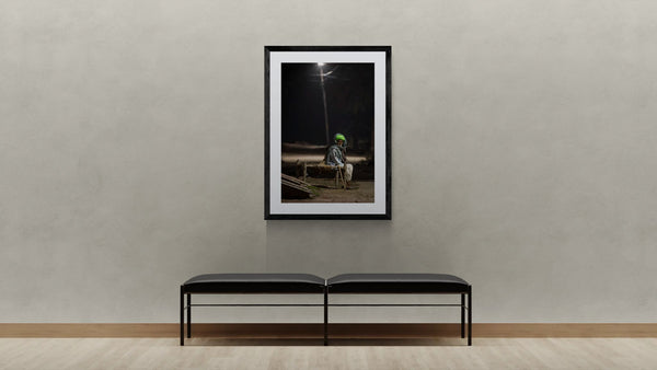 India Man Under Streetlight, Jodhpur framed in black on a gallery wall with a viewer in a straw hat in front — Good Beans NYC.