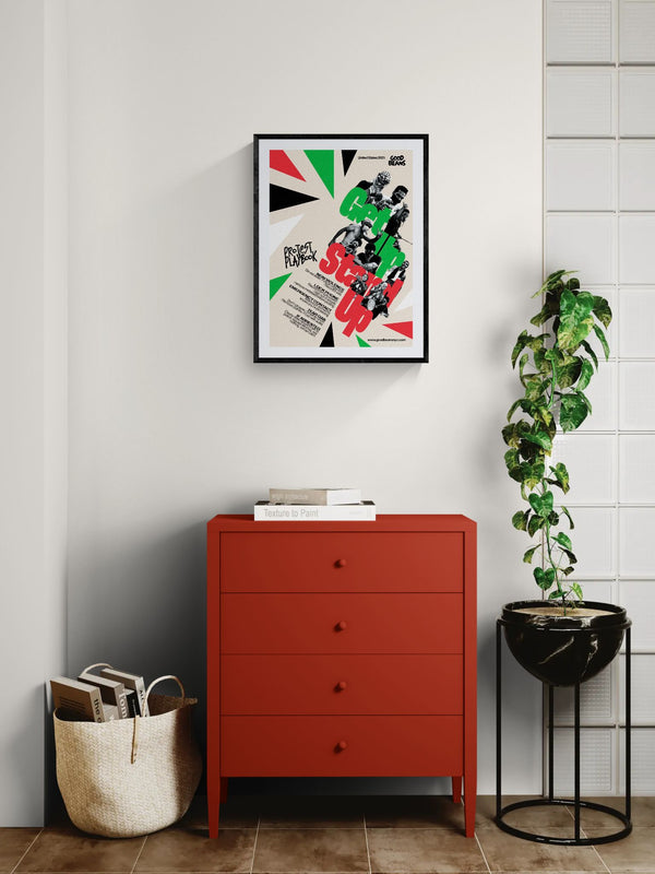 Get In Stand Up Protest Playbook Poster framed in black on a gallery wall with a viewer in a straw hat in front — Good Beans NYC.